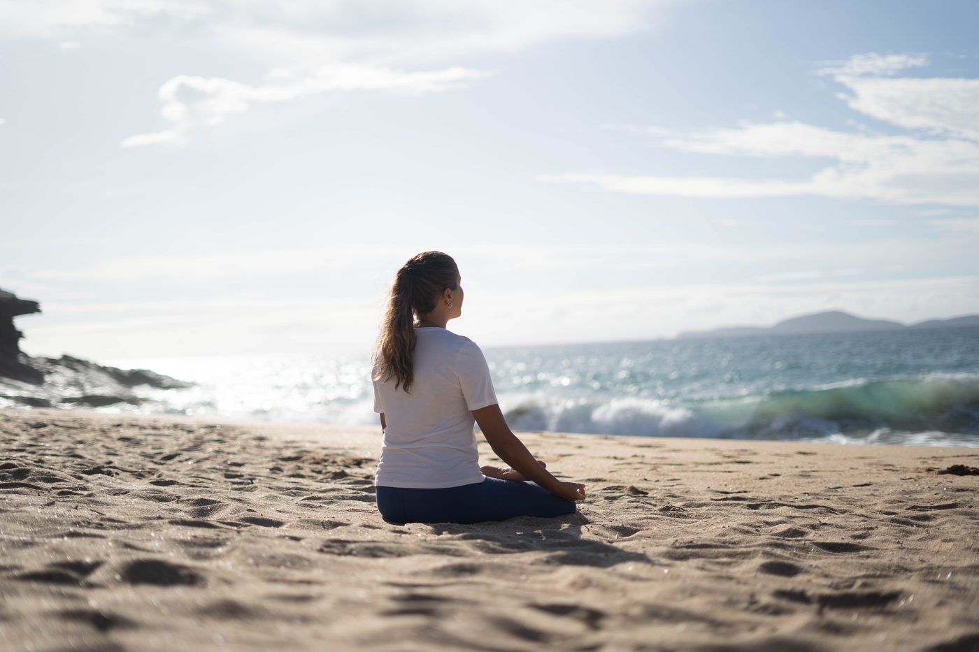 Mulher meditando na praia, de frente para o mar